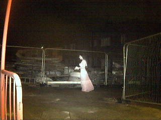 The Limitless Security "ghost". A night time image of a building yard shows a ghostly woman wearing a full length dress. Her skin and the dress are similar shades of eery white and her hair is dark.