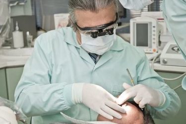 A dentist, in full PPE, examines a patient