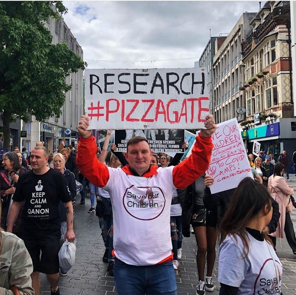 QAnon conspiracy theorists marching in Liverpool, August 2020.

One man wearing a "Save our children UK" T Shirt holds up a placard reading "Research Pizzagate". 

Another man has a "Keep Calm and QAnon t shirt"

Source: https://i.imgur.com/brFk9UX.jpg