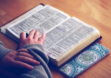 Feminine hands held over a bible, with a pen in one hand as if studying. 