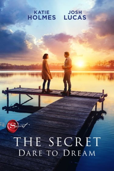 The Secret Dare to Dream promo image. Katie Holmes and Josh Lucas stand on a jetty over a lake with a sunset behind them.