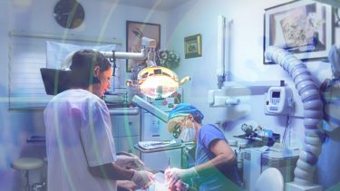 A dentist and her assistant work on a patient's teeth