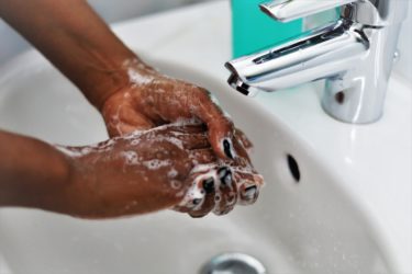 A person with black skin and black nail varnish washes their hands in a sink.