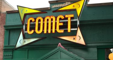 The store front of Comet Ping Pong, the pizza place at the centre of the Pizzagate conspiracy theory. The store is painted dark green and has the word "comet" written in lighted yellow letters. Image by DOCLVHUGO [CC-by-4.0]