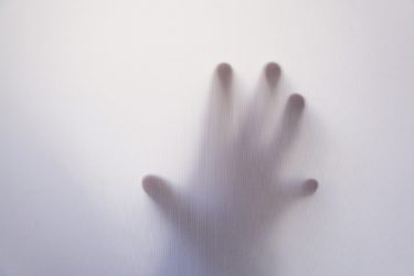 A hand silhouetted against a white sheet as if "from beyond".