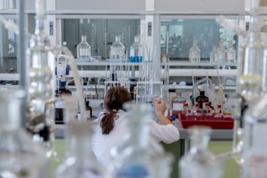 A scientist working in a laboratory. She is wearing a white labcoat and holding a pipette.