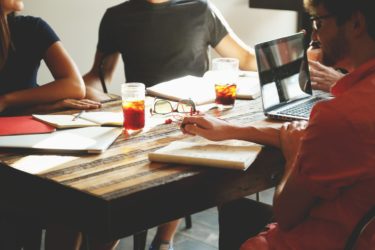 A group of people sat around a table with laptops and notebooks