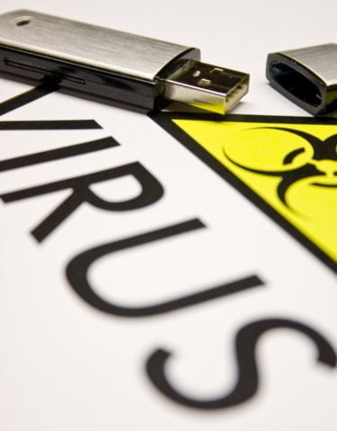 A sheet of white paper with the word Virus and a yellow triangle with a biohazard symbol on it. There is a USB pen sitting on top of the paper. 