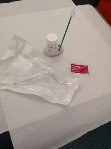 Photo by Florence Schechter shows a plastic speculum in plastic packaging, a smear brush which is used to scrape the cells from the cervix, a sample pot and a small sachet of lubricant.