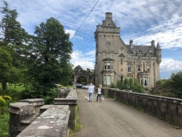 Overtoun Bridge approaching Overtoun House. Two dog walkers with small white dogs are walking towards the house. Photo by Dave Souza (CC BY-SA 4.0) https://commons.wikimedia.org/wiki/File:Overtoun_Bridge_-_approach_to_Overtoun_House.jpg