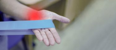 A person holds a resistance band with their hand - a red spot indicates the pain they feel in their wrist