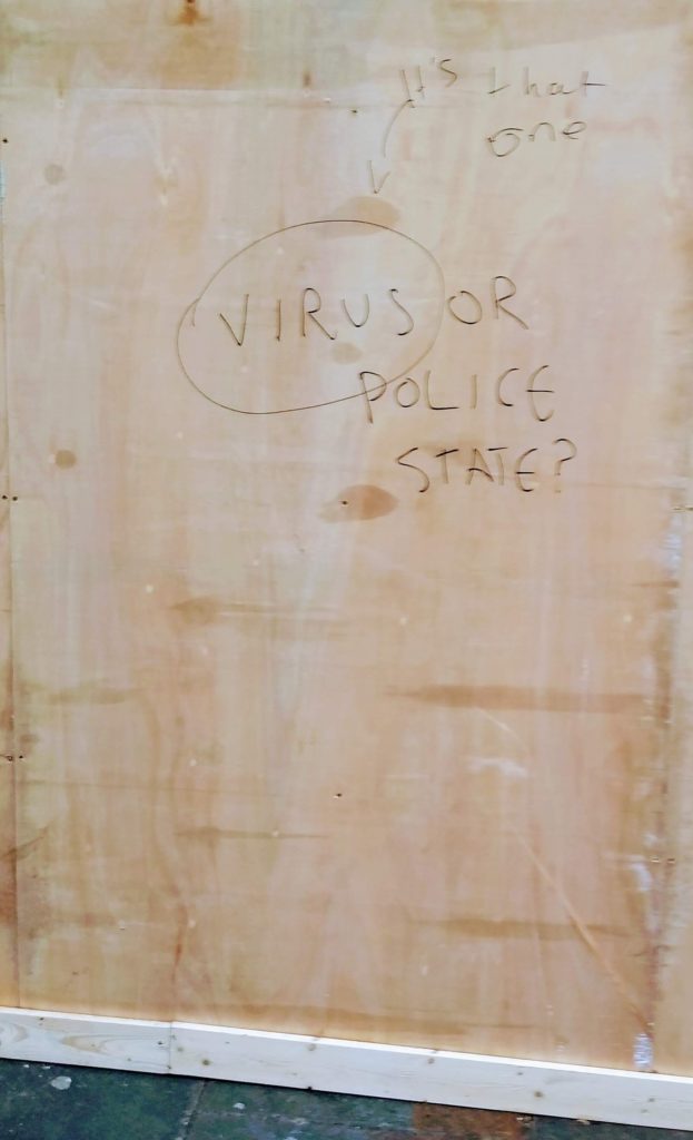 A piece of wood which has the words "Virus or police state" written on it. A second person has circled the word "virus" and written "it's that one".