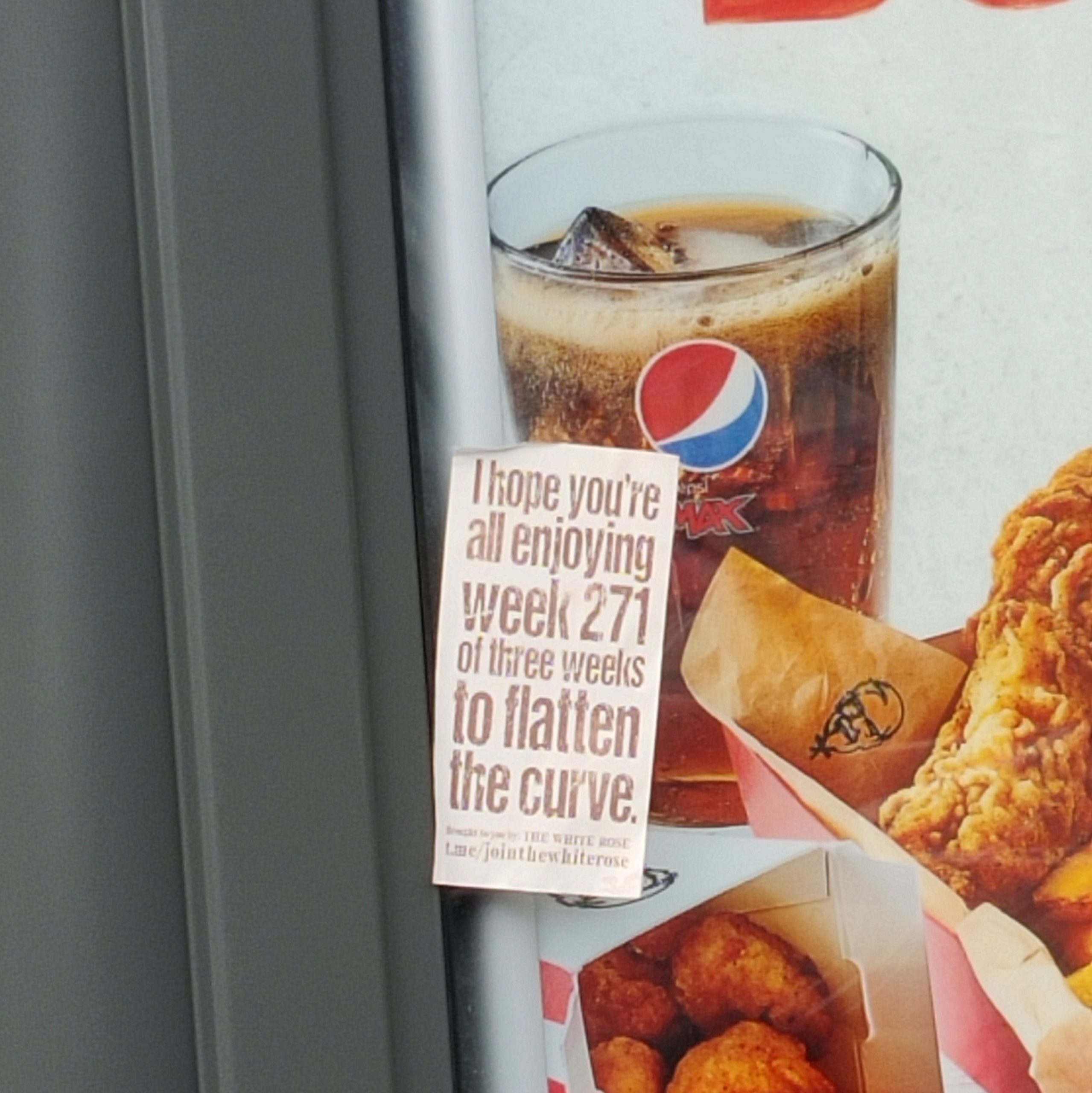 A White Rose sticker on a bus stop advert for fried chicken. The sticker reads "I hope you're all enjoying week 271 of three weeks to flatten the curve" - in small print below are adverts for the White Rose Telegram group.