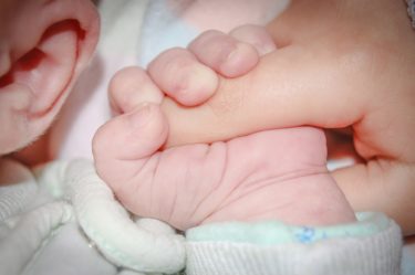 A newborn baby holding its mother's finger
