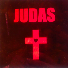 The cover of Lady Gaga's Judas - a dark background with the word JUDAS in large red writing. Beneath is a red cross with a heart in the centre. 