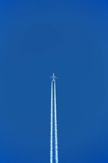 A plane flying on a blue sky with two white contrails following it