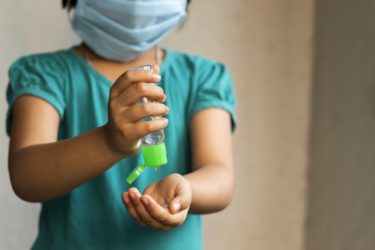 A young child wearing a face mask and sanitising their hands