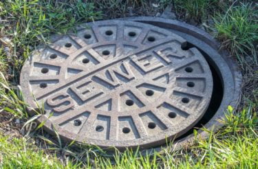 A maintenance hole cover in the grass labelled "sewer".