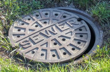 A maintenance hole cover in the grass labelled "sewer". 