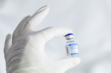 A gloved hand holding a vaccine ampoule