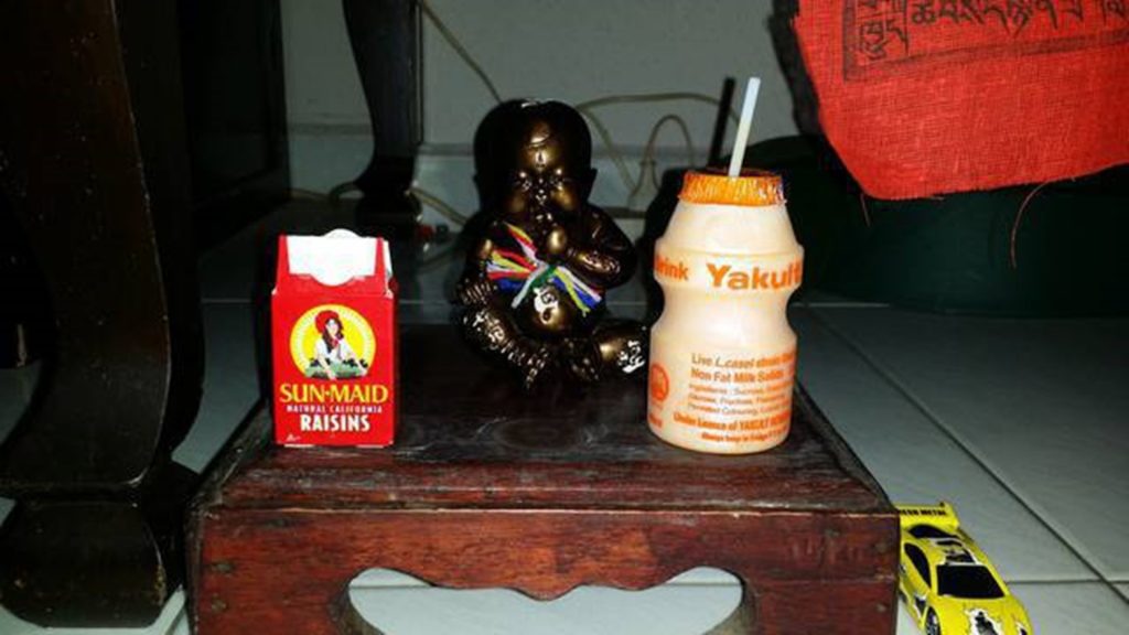 A shrine made by user okliao75 for his newly purchased Kumanthong, it contains a packet of raisins, Yakult and a toy car as offerings. Source: Amulet Forums