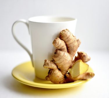 A tea cup with some fresh ginger propped up beside it. 