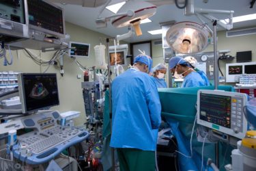 Surgeons in a surgery theatre working on a patient who is behind a screen