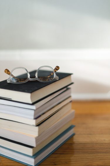 A stack of 8 books with a pair of glasses on top. 