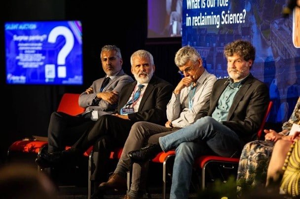 The panel of four men on stage with a woman sitting beside them mostly out of shot