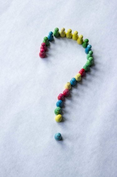 A question mark made up of board game character meeple of mixed colours on a white background.