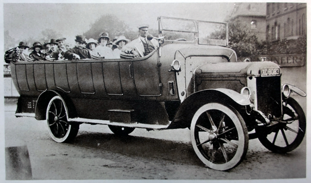 An old photograph of a Charabanc, filled with people wearing hats. The Charabanc is described in the main text as a large open top vehicle with rows of benches to seat many people. 