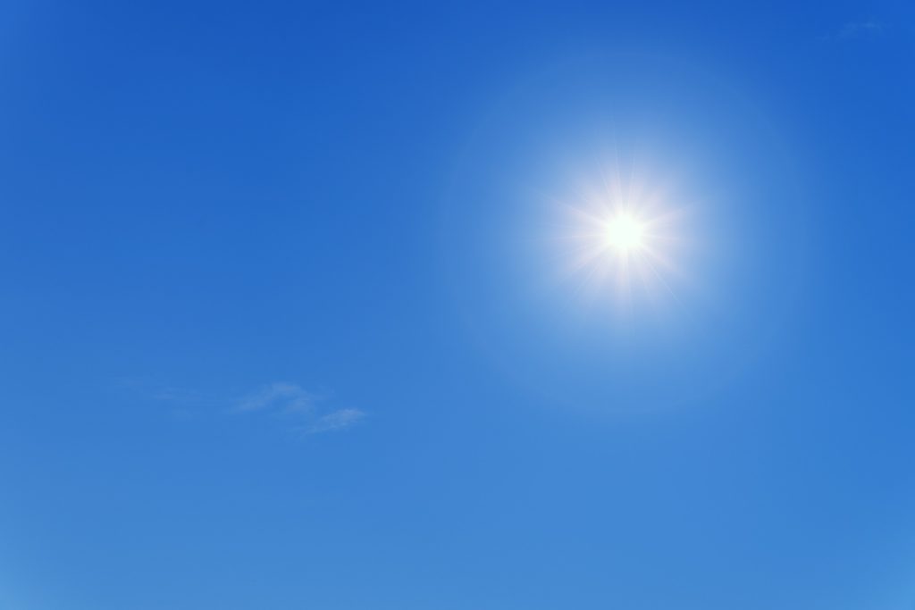 A shining sun in a blue sky, with a wisp of cloud