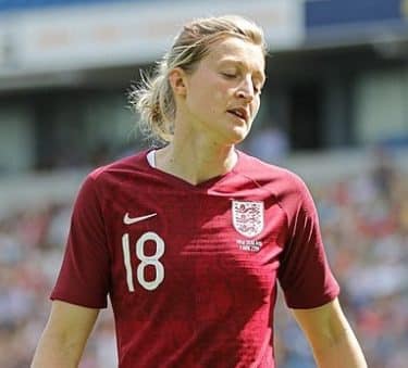 Ellen White on a football pitch wearing a red England football team shirt and with her blonde hair tied in a low ponytail. 