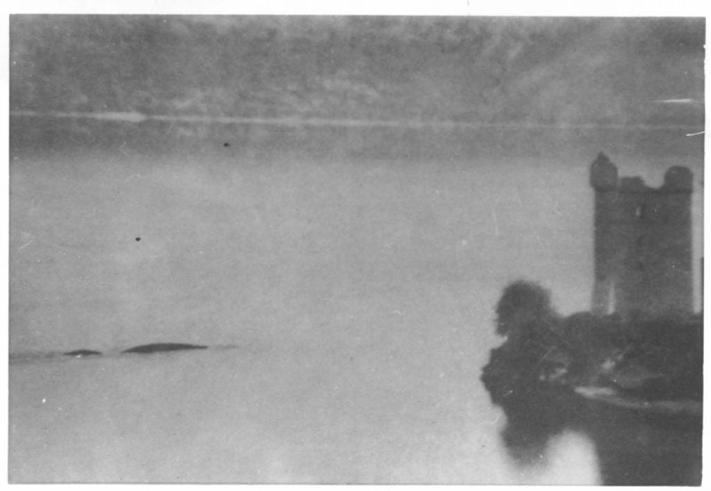 A loch with a castle. On the left, in the water, are two dark bumps. 