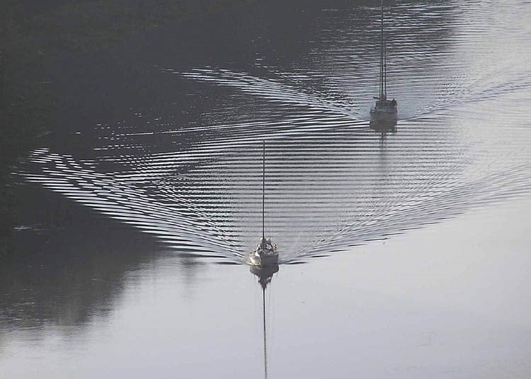 Two boats with wide wakes behind them. 