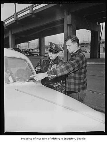 Man showing pitted windshield to police officer, Seattle, 1954
