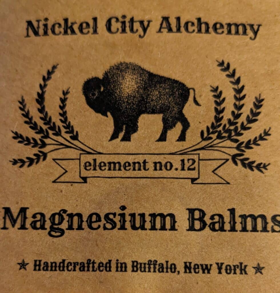 The branding for "Nickel City Alchemy Magnesium Balms" which has a buffalo in the centre and reads "element no. 12". 