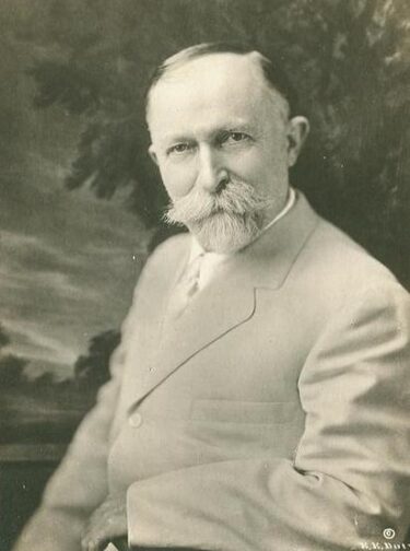 A photograph of Henry Kellogg - a white man with short grey hair and a grey wiry beard and moustache. He is wearing a light coloured suit. 

Source: https://en.wikipedia.org/wiki/File:Portrait_of_Dr._John_Harvey_Kellogg.jpg

Public domain