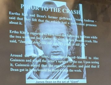 Slide with text over a black and white image of James Dean wearing a cowboy hat, titled "PRIOR TO THE CRASH". It reads "Eartha Kitt and Dean's former girlfriend Ursula Andress - said that they felt that the vehicle had a malevolent presence about it. 
Ertha Kitt [sic] is reported to have said the following to Dean while the two were out for a drive the week before Dean's crash. She said, "James, I don't like this car, it's going to kill you,"
Around the same time, Dean introduced himself to Alec Guinness and asked the actor's opinion of the car. Upon seeing it, Guinness stated that the car was sinister, and said that if Dean got into it, he would be dead within the week." The photo is captioned "James Dean on the set of 'Giant'".
Source: Brian Eggo