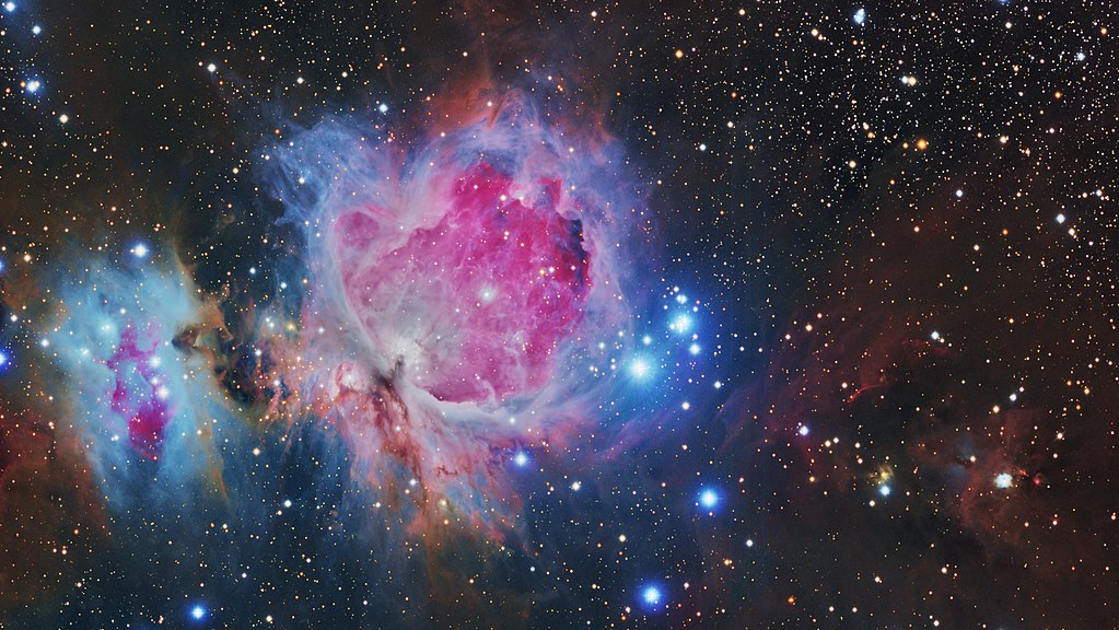 HDR image of the Orion Nebula and 'Running man', surrounded by other distant stars and galaxies. A range of dust colours in the nebula are visible; orange, blue, pink, purple and more.