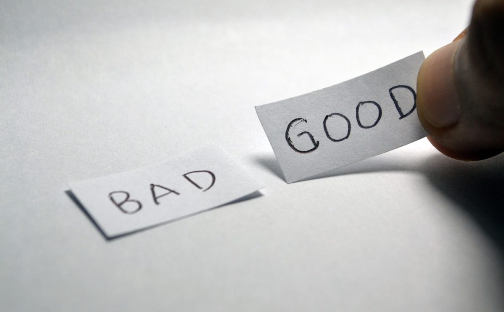 A hand picking up a small white piece of paper with GOOD written on it, which is lying on a white surface next to another piece that says BAD.