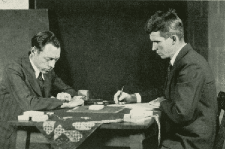 A black and white photo of Hubert Pearce and J.B. Rhine experimenting with Zener cards. Rhine is holding a pen in his right hand. Both men look serious, wearing suits, staring at the table.