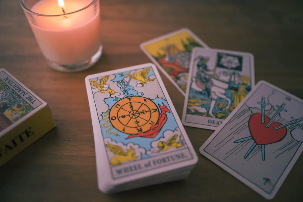 A deck of tarot cards with a few spread out on a table, by a lit candle in a glass holder
