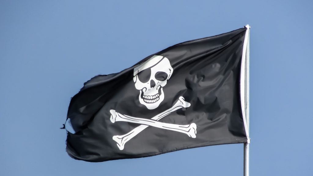 A black flag with an eye-patched skull and crossbones in white, flying against a blue sky - the quintessential pirate flag