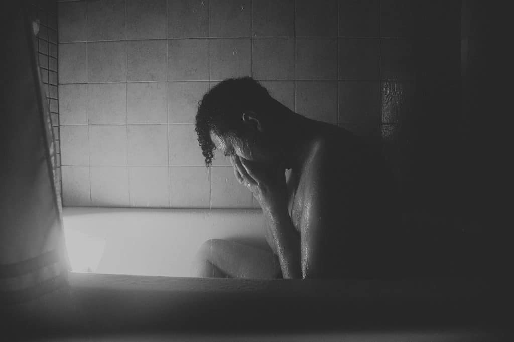 A man sits alone in a bathtub, distressed.