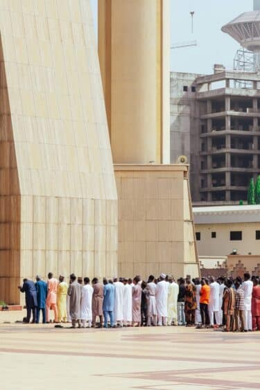 People gathered outside a huge yellow stone building. They are dwarfed by the buildings scale.