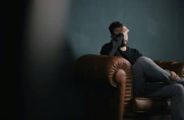 A white man sitting on a sofa with his head in his hand. 

Photo by Nik Shuliahin 💛💙 on Unsplash




