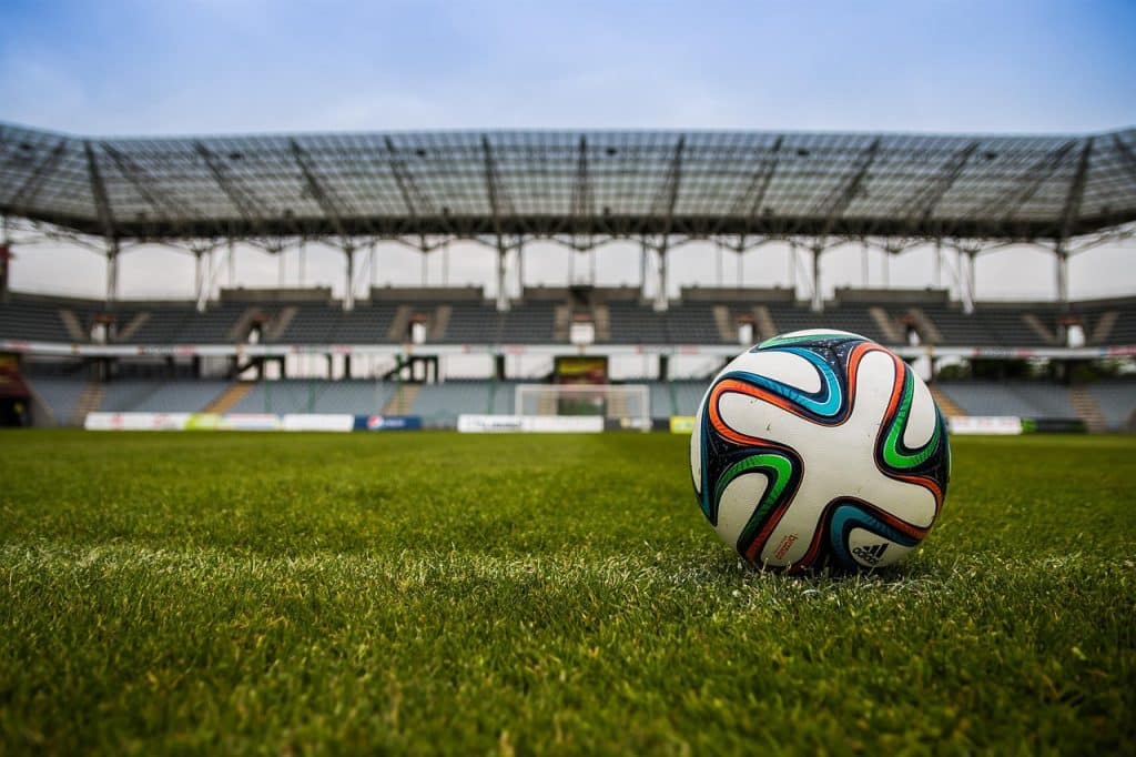 A football sitting on the pitch with stadium stands visible in the background