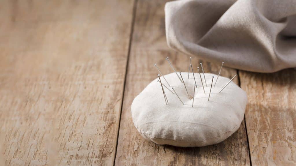 A pin cushion on a wooden table, with several pins protruding 