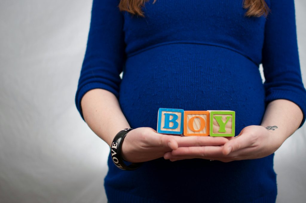 Three blocks spelling the word "BOY" are held in front of a pregnancy bump.